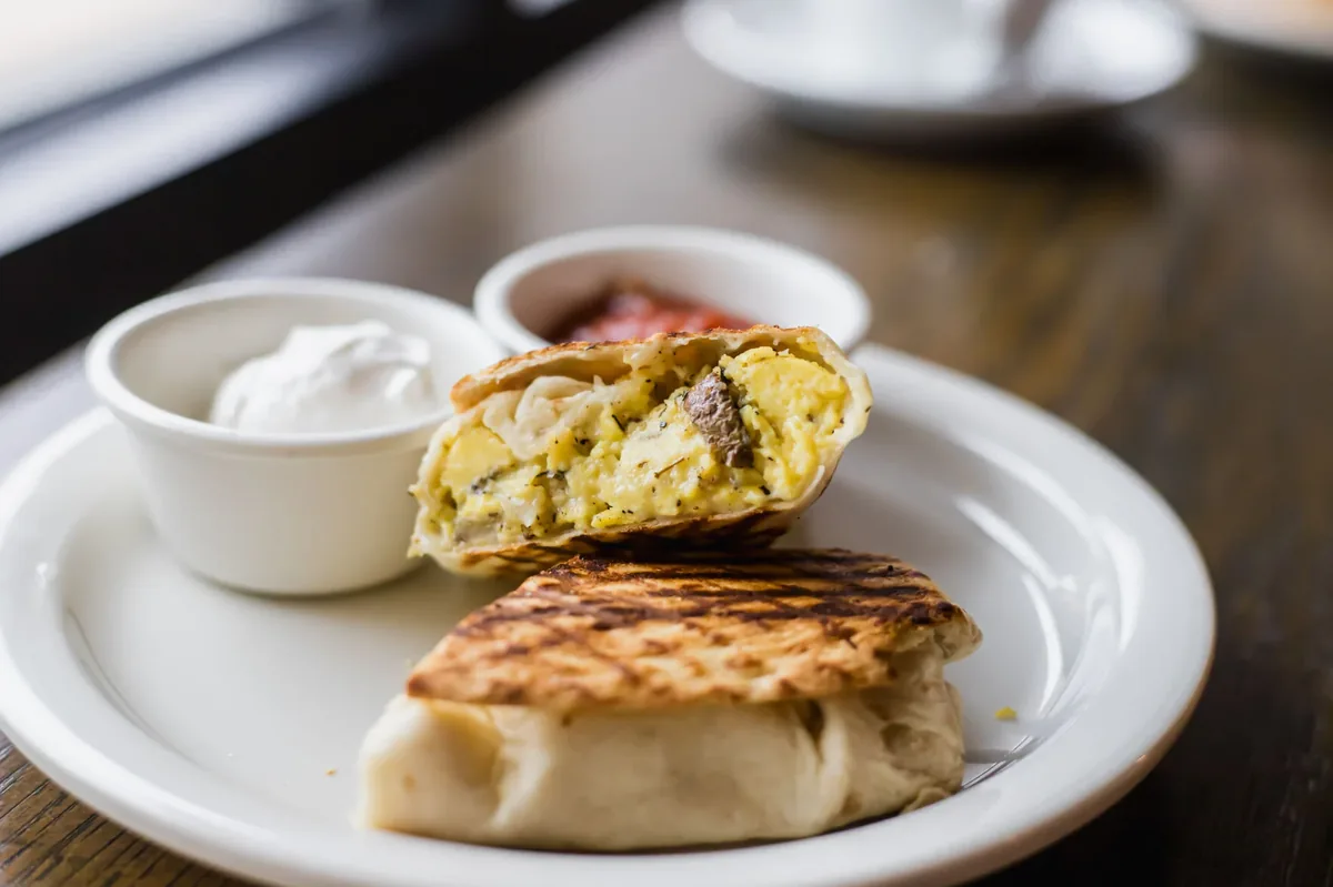 A grilled breakfast burrito with eggs, cut open on a plate