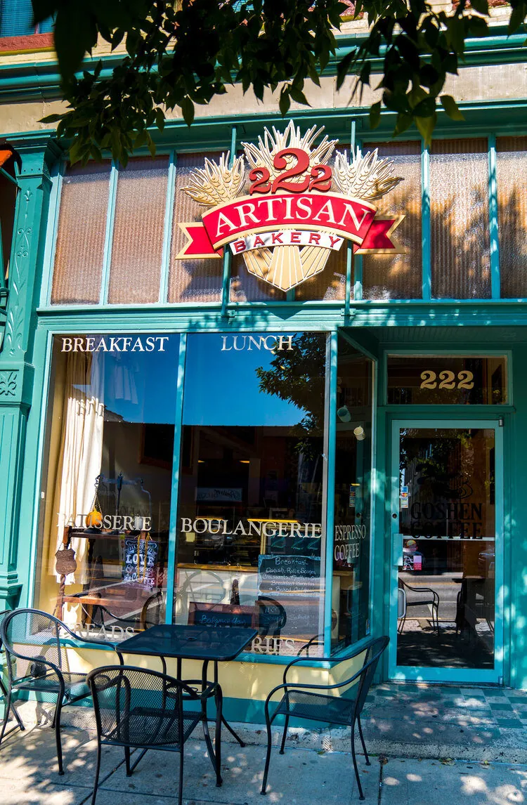 The 222 Artisan Bakery storefront in Edwardsville with its carved sign, gilt BREAKFAST and LUNCH lettering, and a bistro table out front
